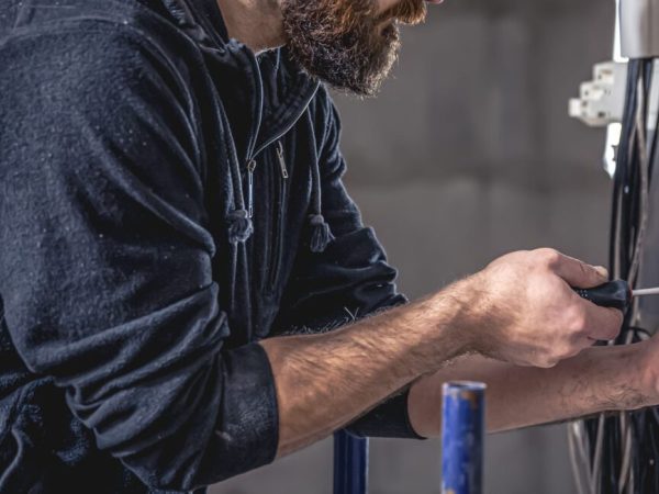 a male electrician works in a switchboard with an electrical connecting cable.