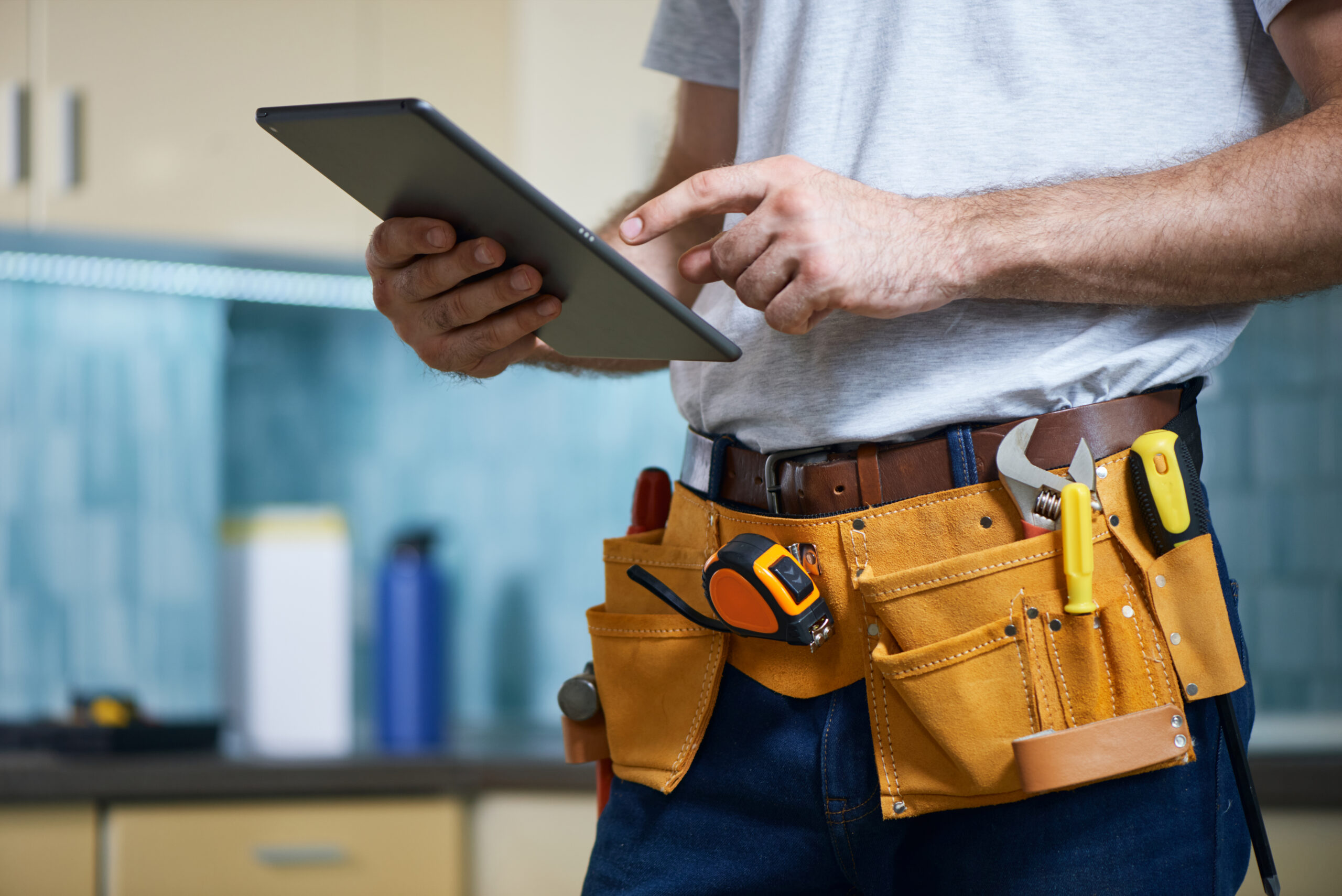 cropped shot of young repairman wearing a tool belt with various tools using digital tablet while standing indoors
