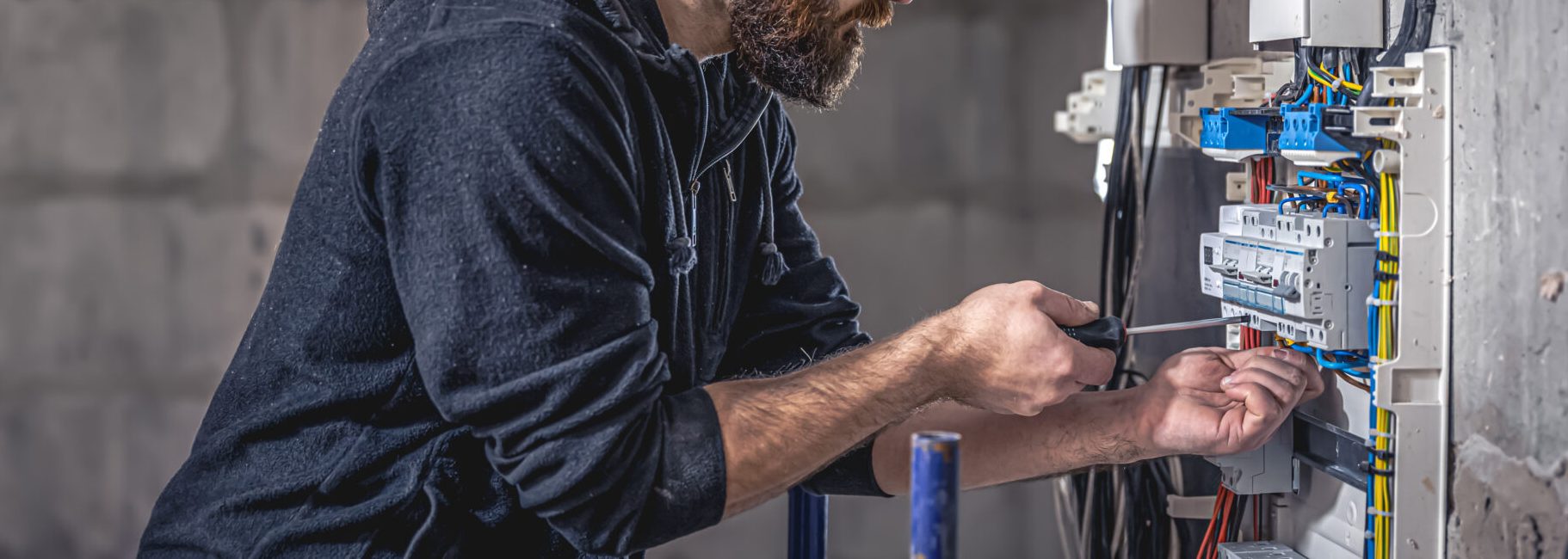 a male electrician works in a switchboard with an electrical connecting cable.