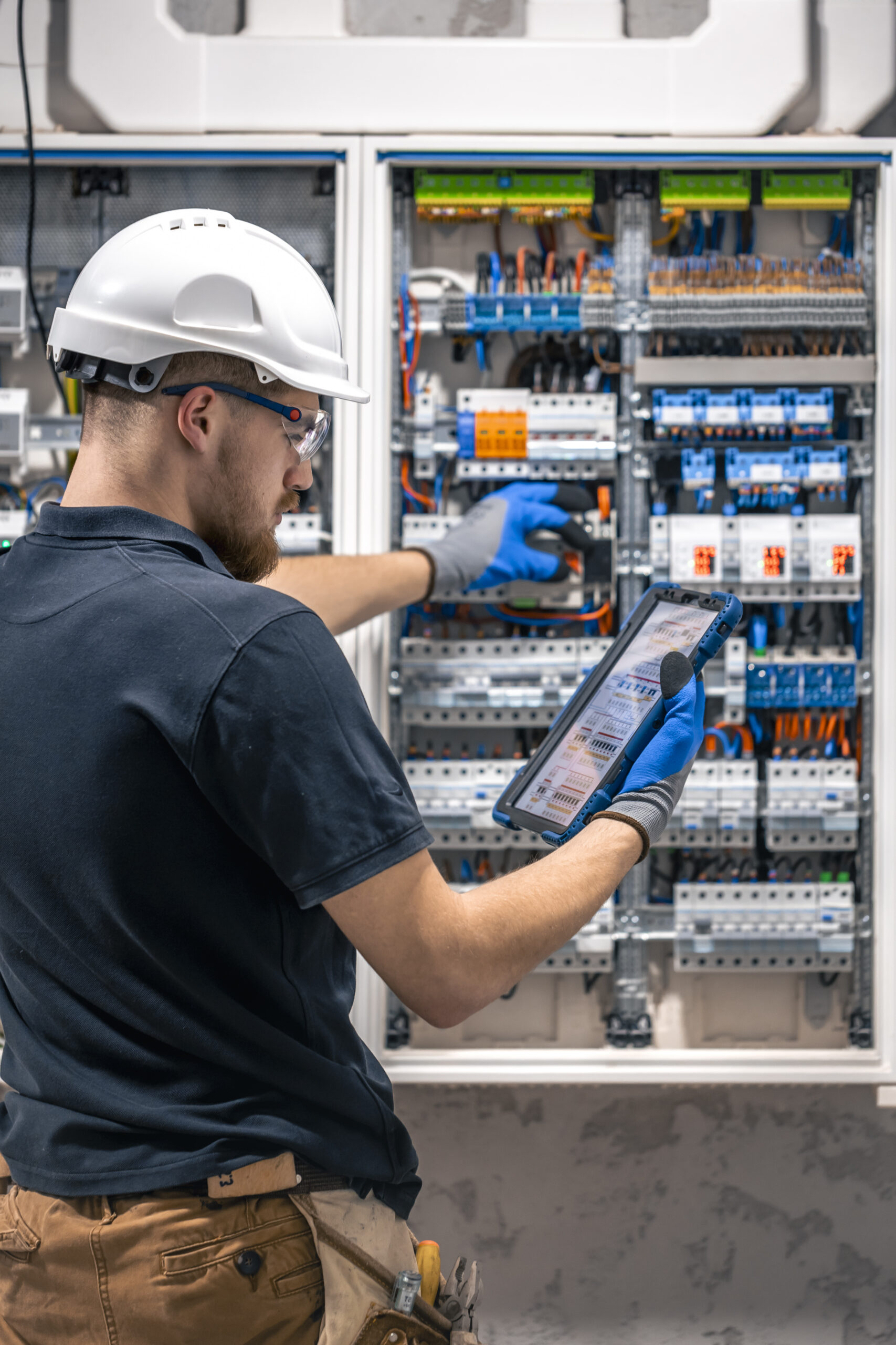 electrical technician working in a switchboard with fuses, uses a tablet.